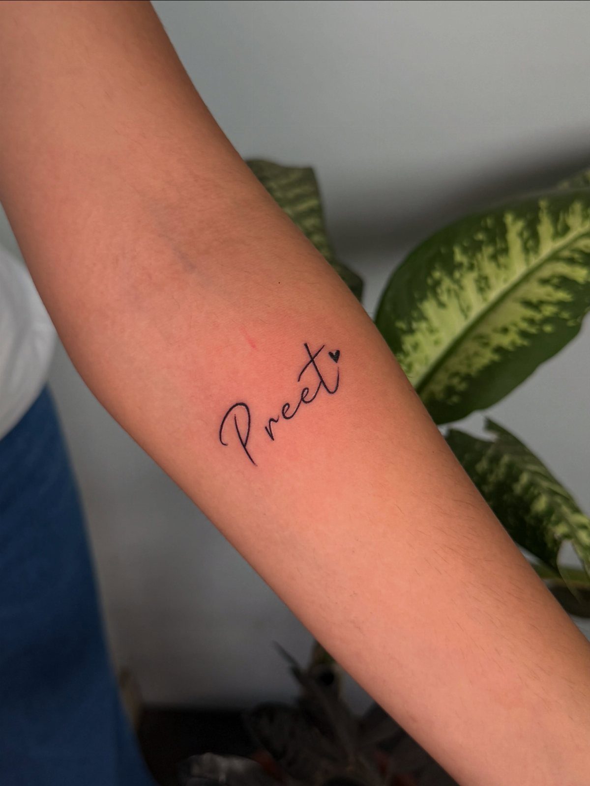 Cursive name tattoo reading Preet with a small heart on a forearm