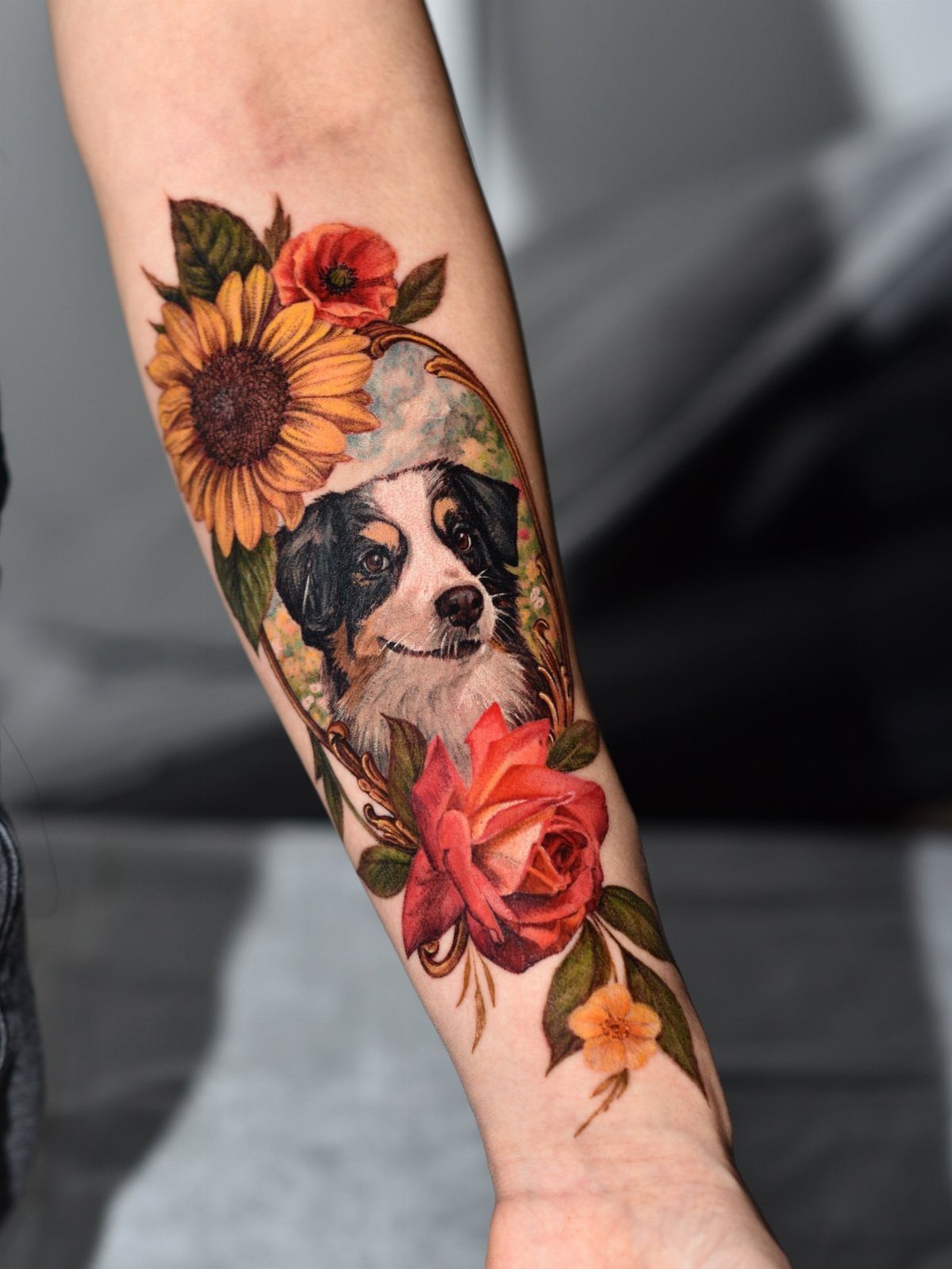Colorful forearm tattoo of a dog portrait framed by sunflowers and red roses.