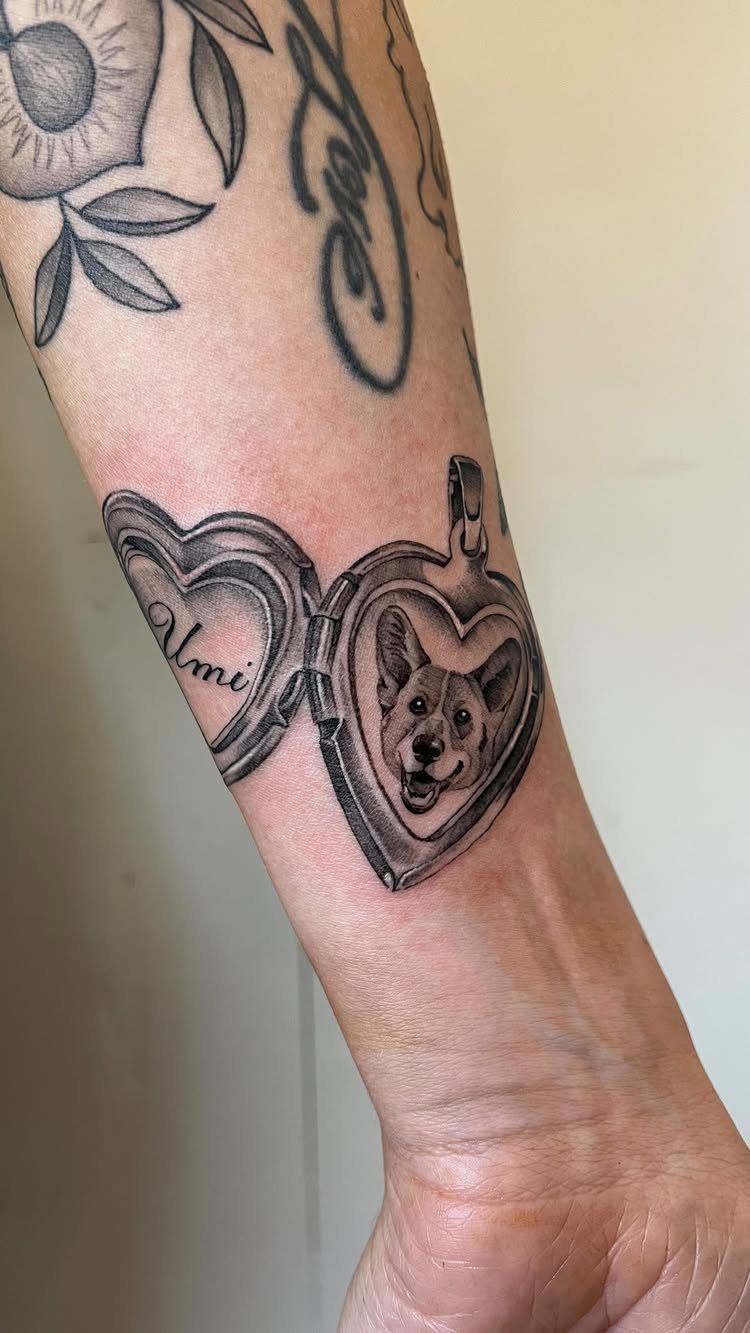 Heart-shaped locket tattoo on a forearm containing a realistic portrait of a dog.