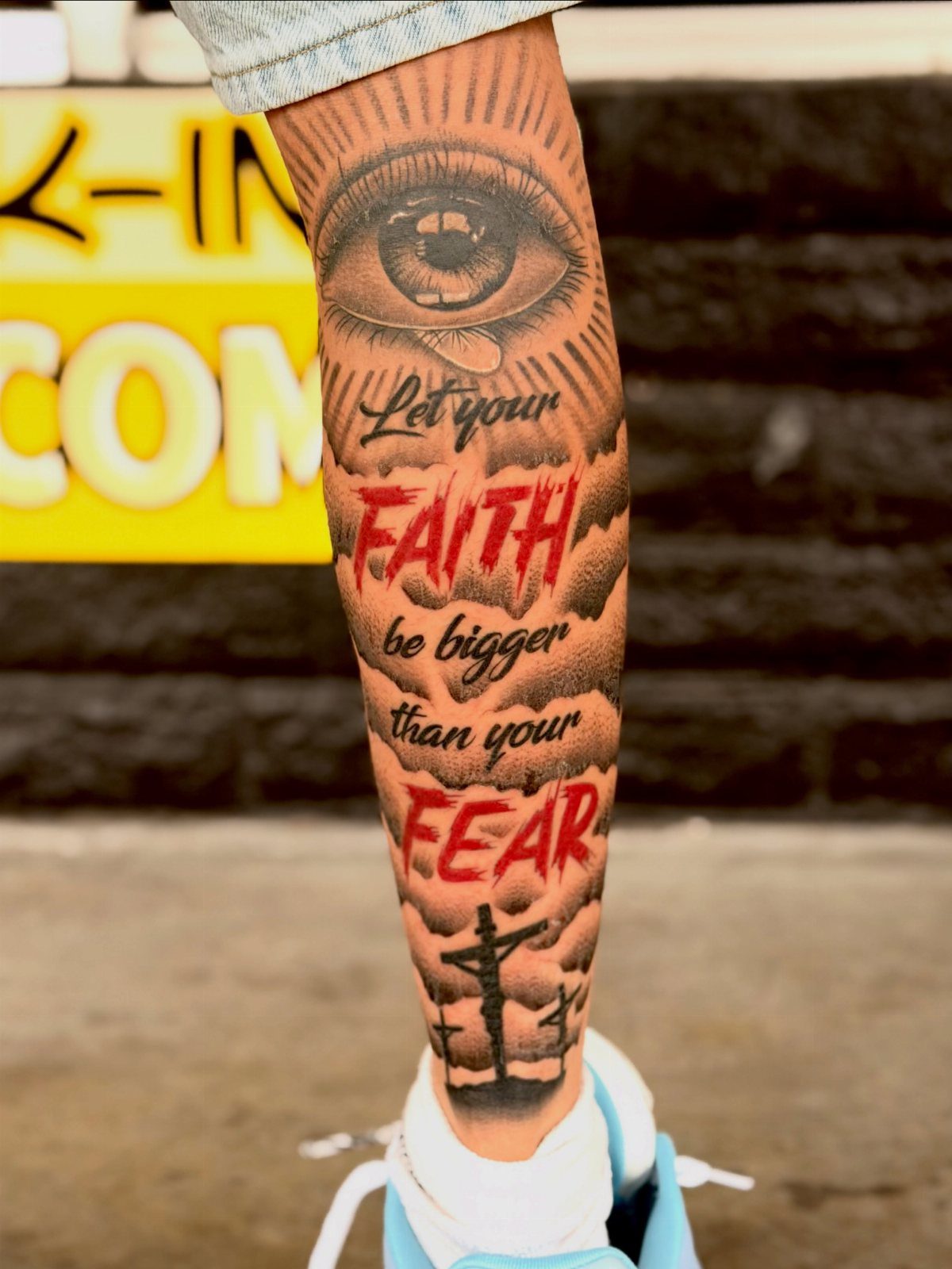 Leg tattoo featuring an eye, faith over fear text, and a small cross.