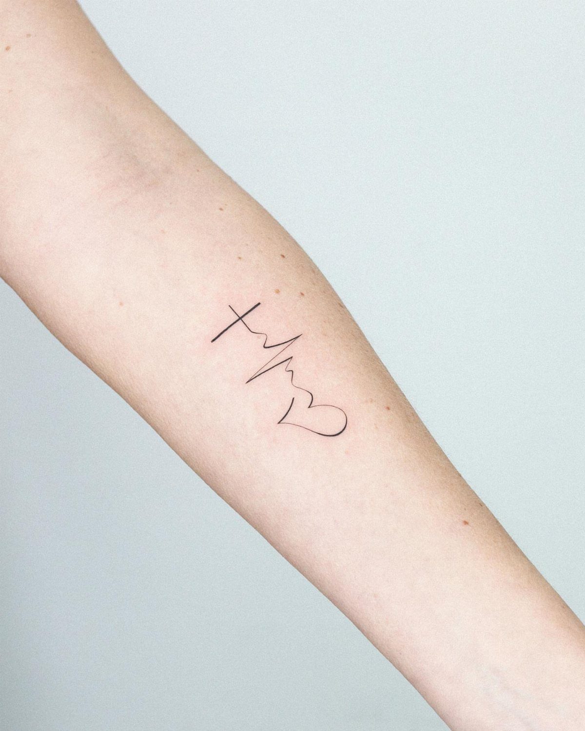Heartbeat cross tattoo on a forearm with an EKG line and heart.