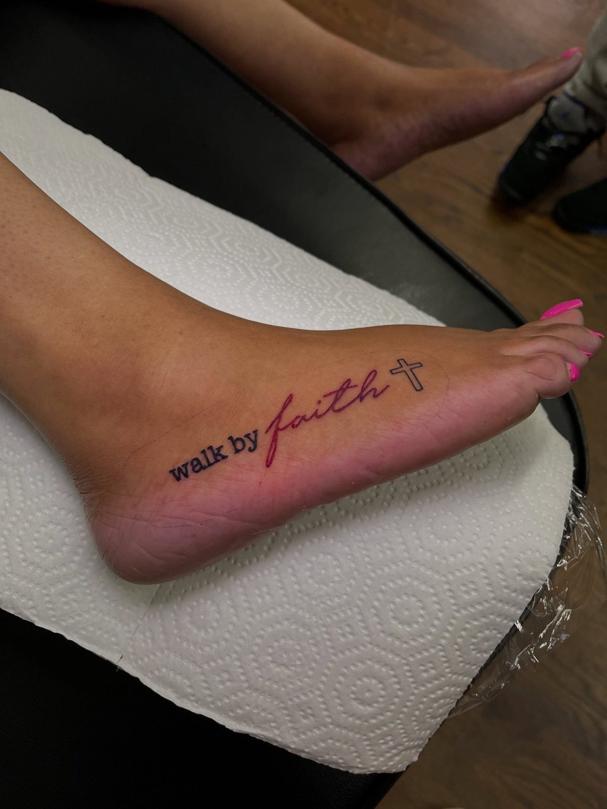 Tattoo on a foot featuring the words walk by faith and a cross.