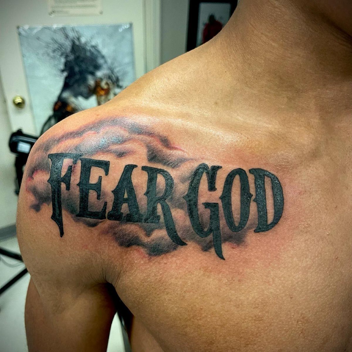 Fear God tattoo in gothic lettering with smoke shading on a man's chest.
