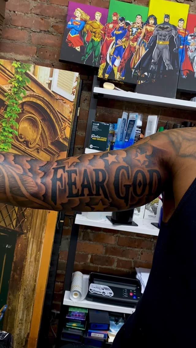 Forearm tattoo with the words Fear God in bold black stylized lettering.
