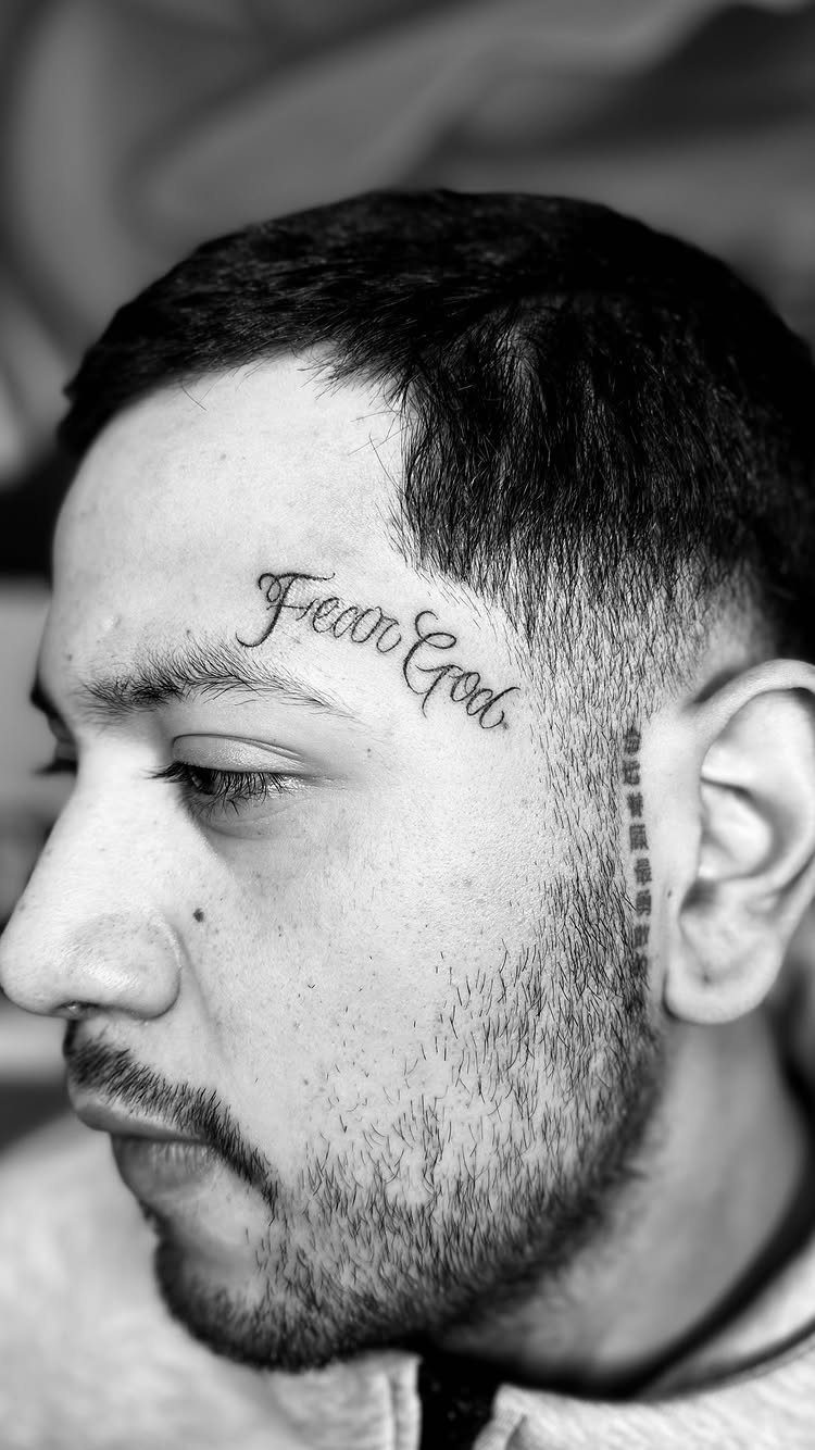 Man with a cursive Fear God tattoo on his forehead in black and white.