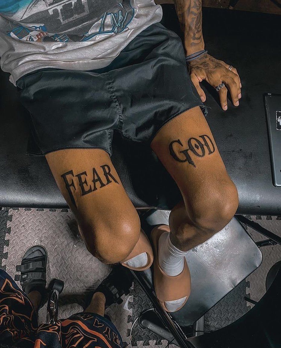Tattoos on a person's thighs reading 'FEAR' and 'GOD' in black ink.