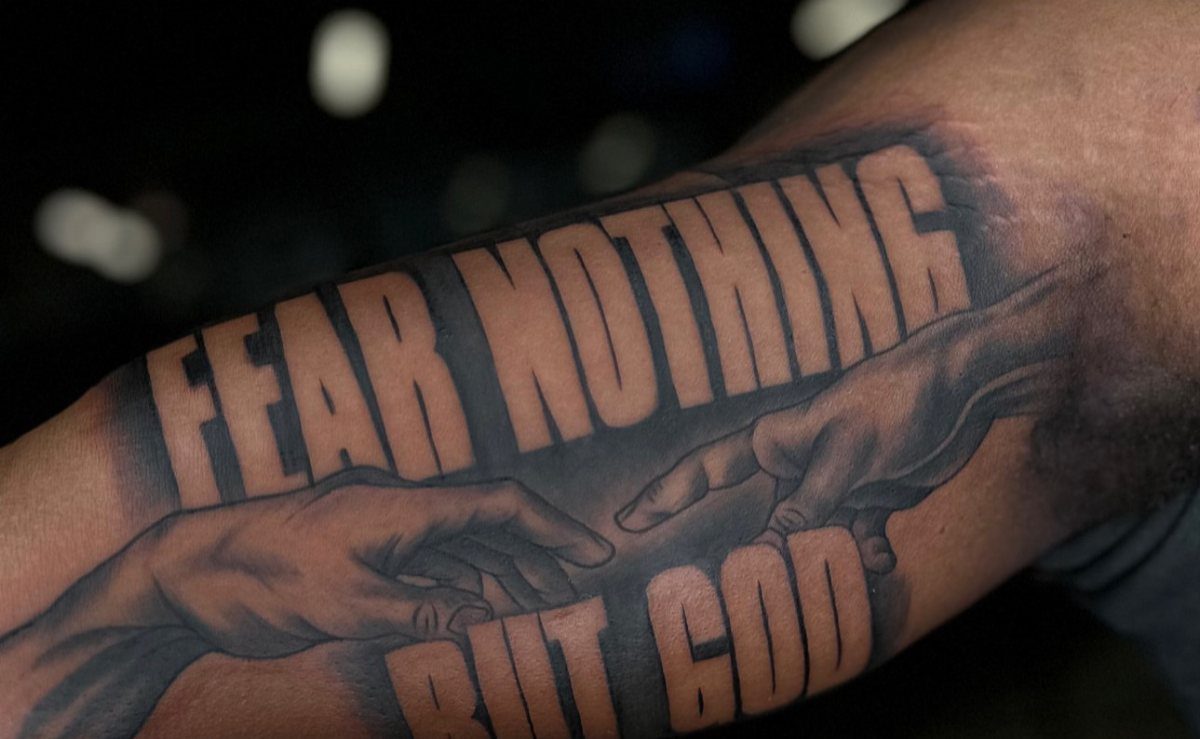 Tattoo on an arm with text Fear Nothing But God and reaching hands.