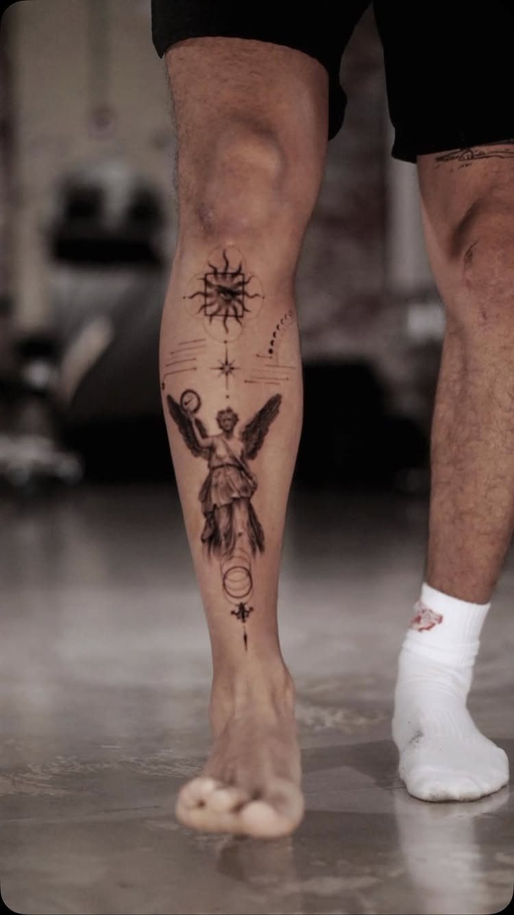 Tattooed lower leg featuring a winged figure and celestial symbols in fine lines.