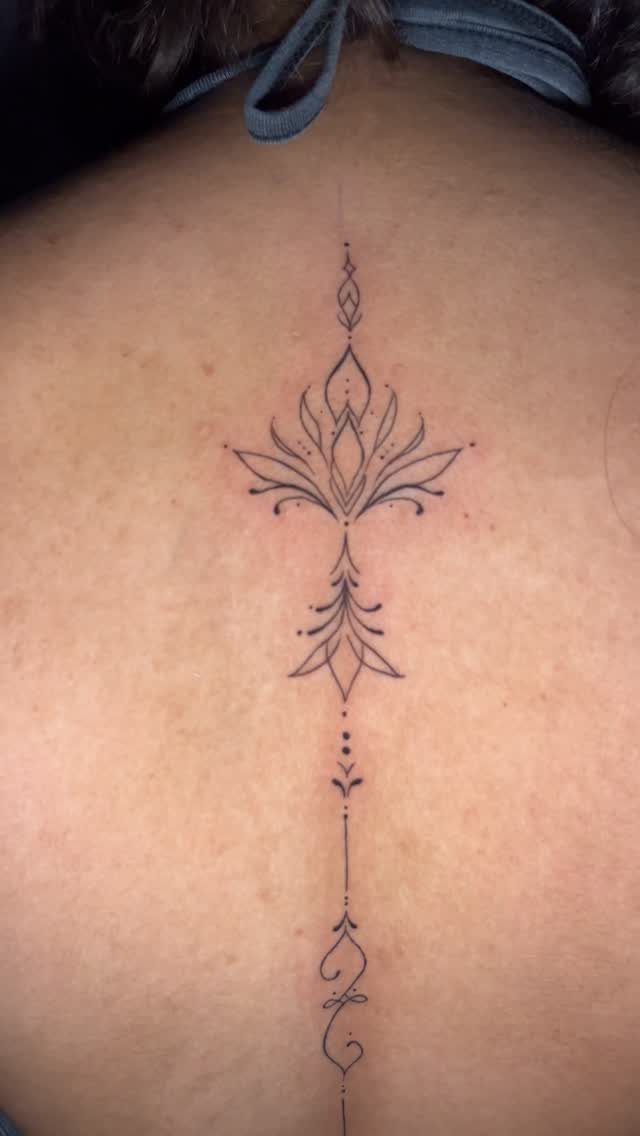 Ornamental fine line tattoo on a back featuring a symmetrical lotus flower design.