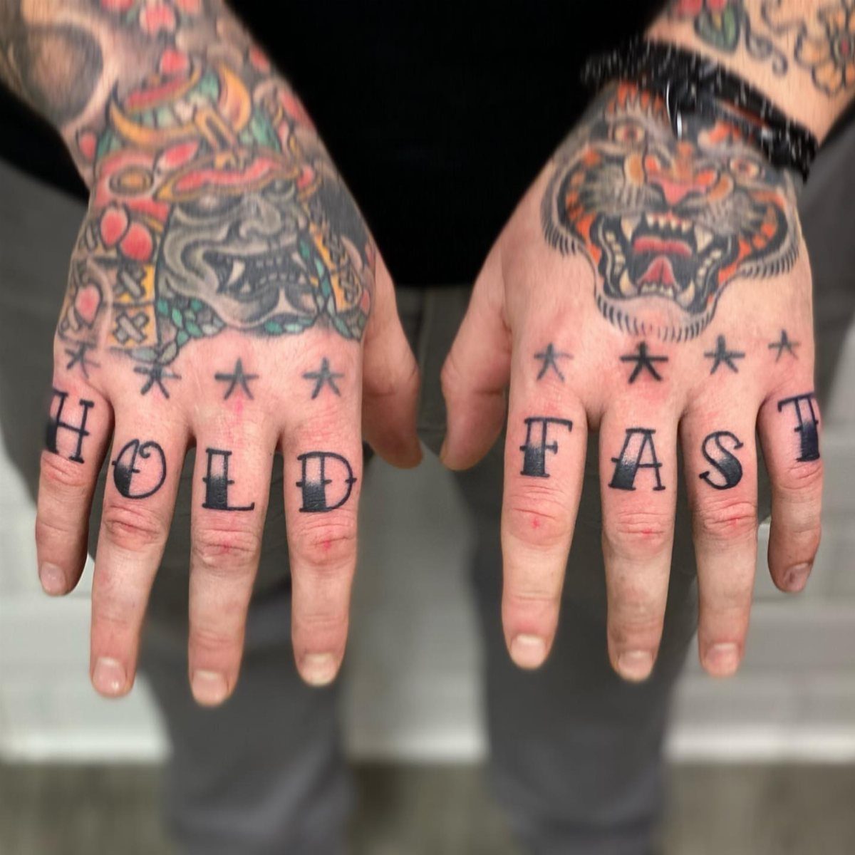Tattooed hands showing the words HOLD FAST across the knuckles with small stars above.
