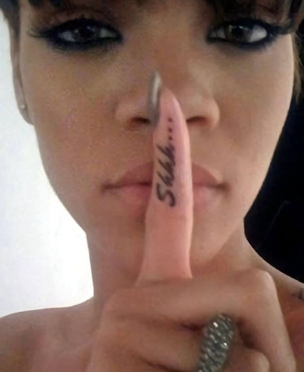 Person shushing with a finger tattoo that reads Shhh on the index finger