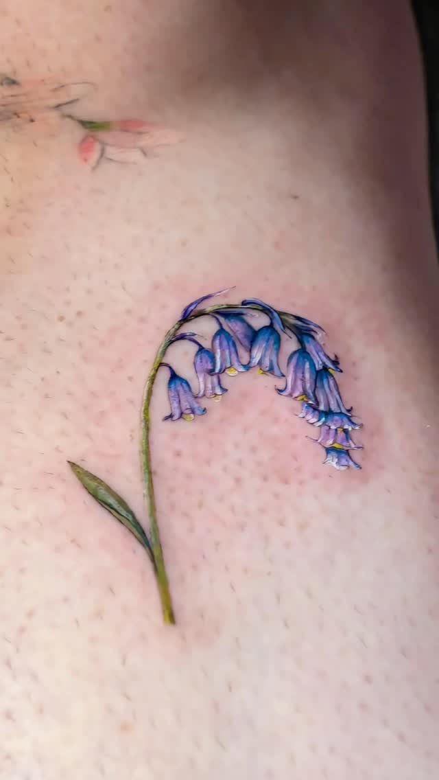 Bluebell flower tattoo with detailed purple petals and green stem on pale skin.