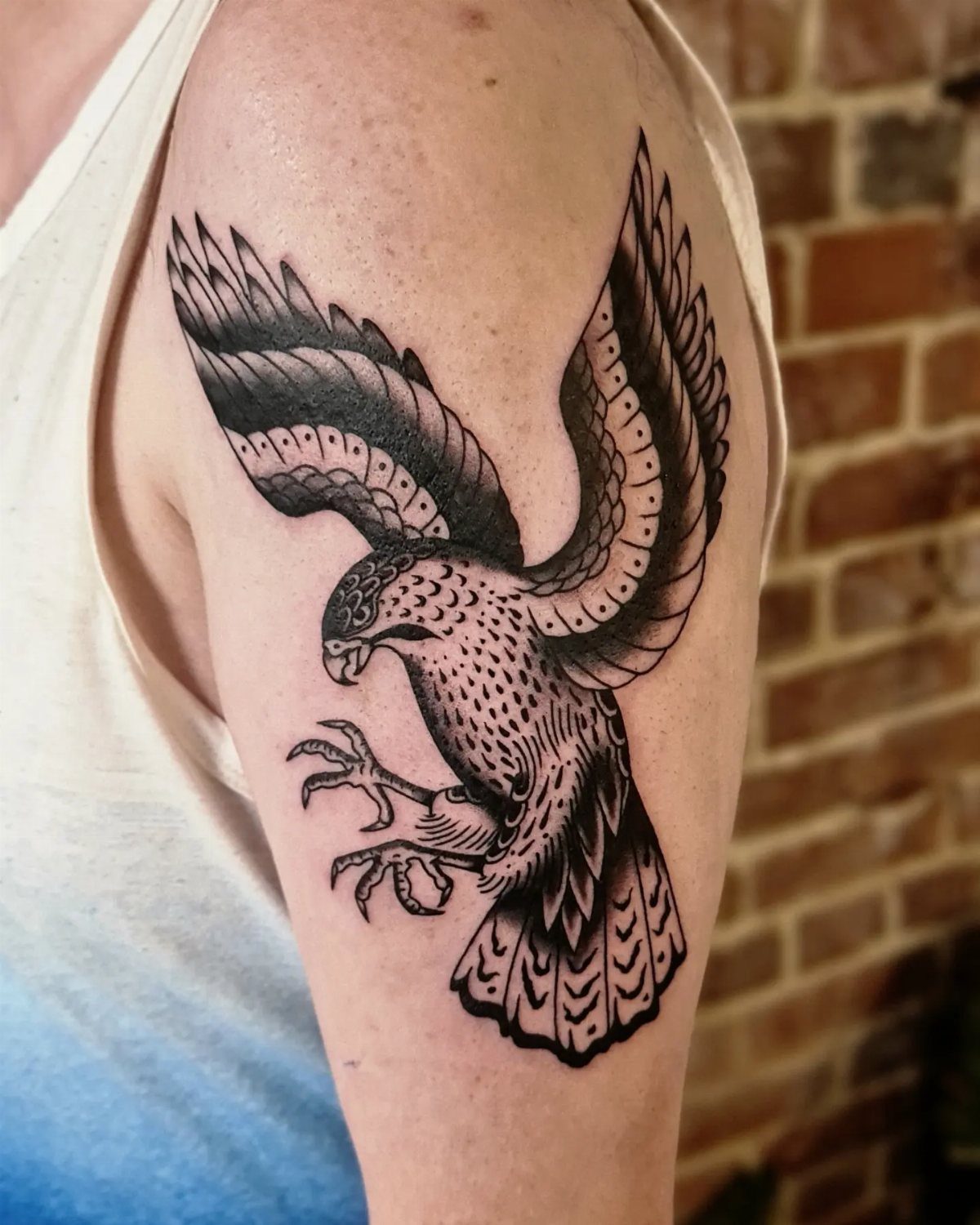 Black ink hawk tattoo with outstretched wings on a person's upper arm