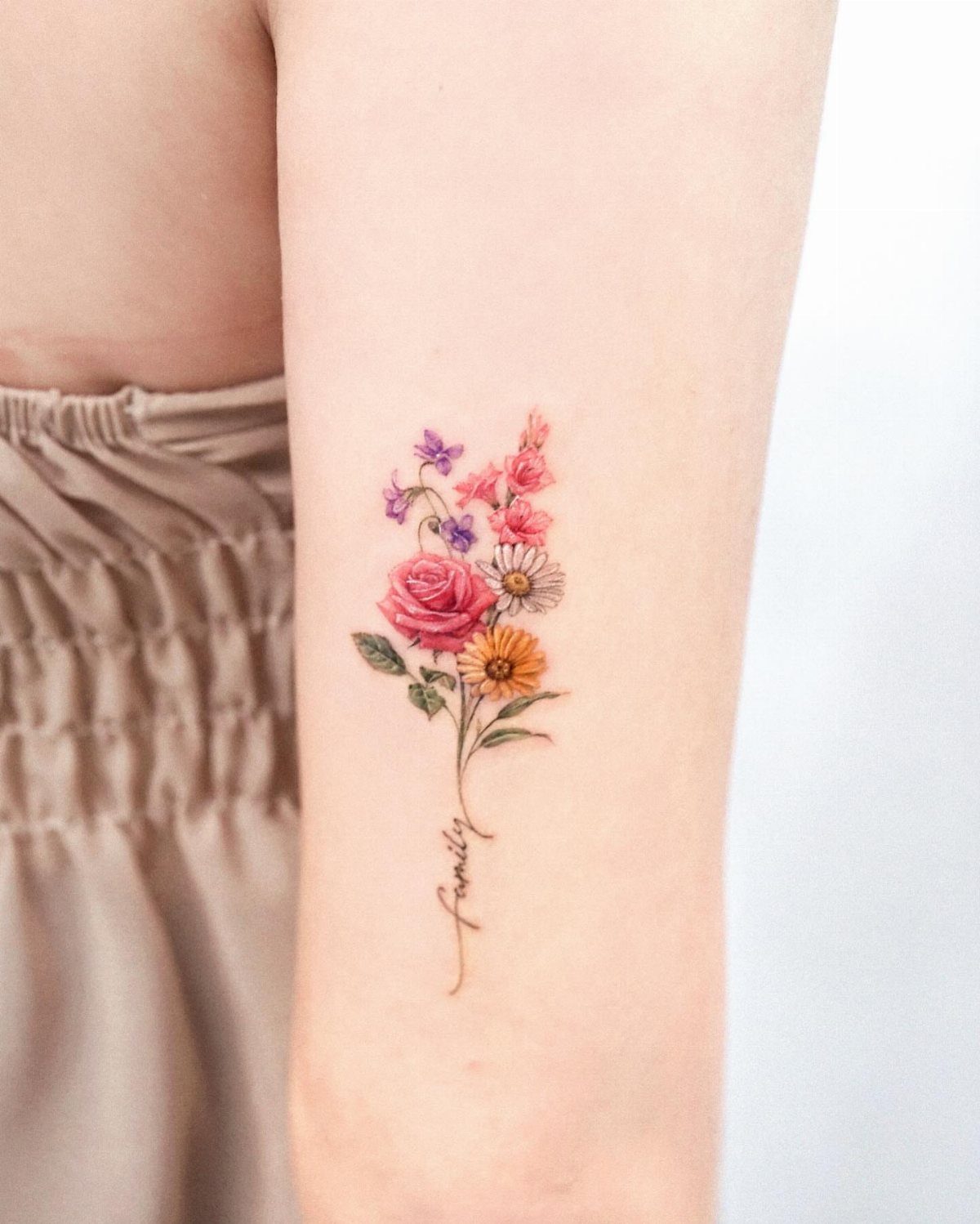 Colorful floral bouquet tattoo on a forearm with the word family as the stem