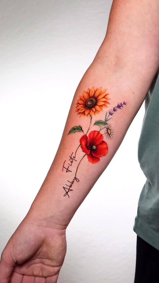Floral bouquet tattoo on forearm with a sunflower, poppy, and two cursive names.