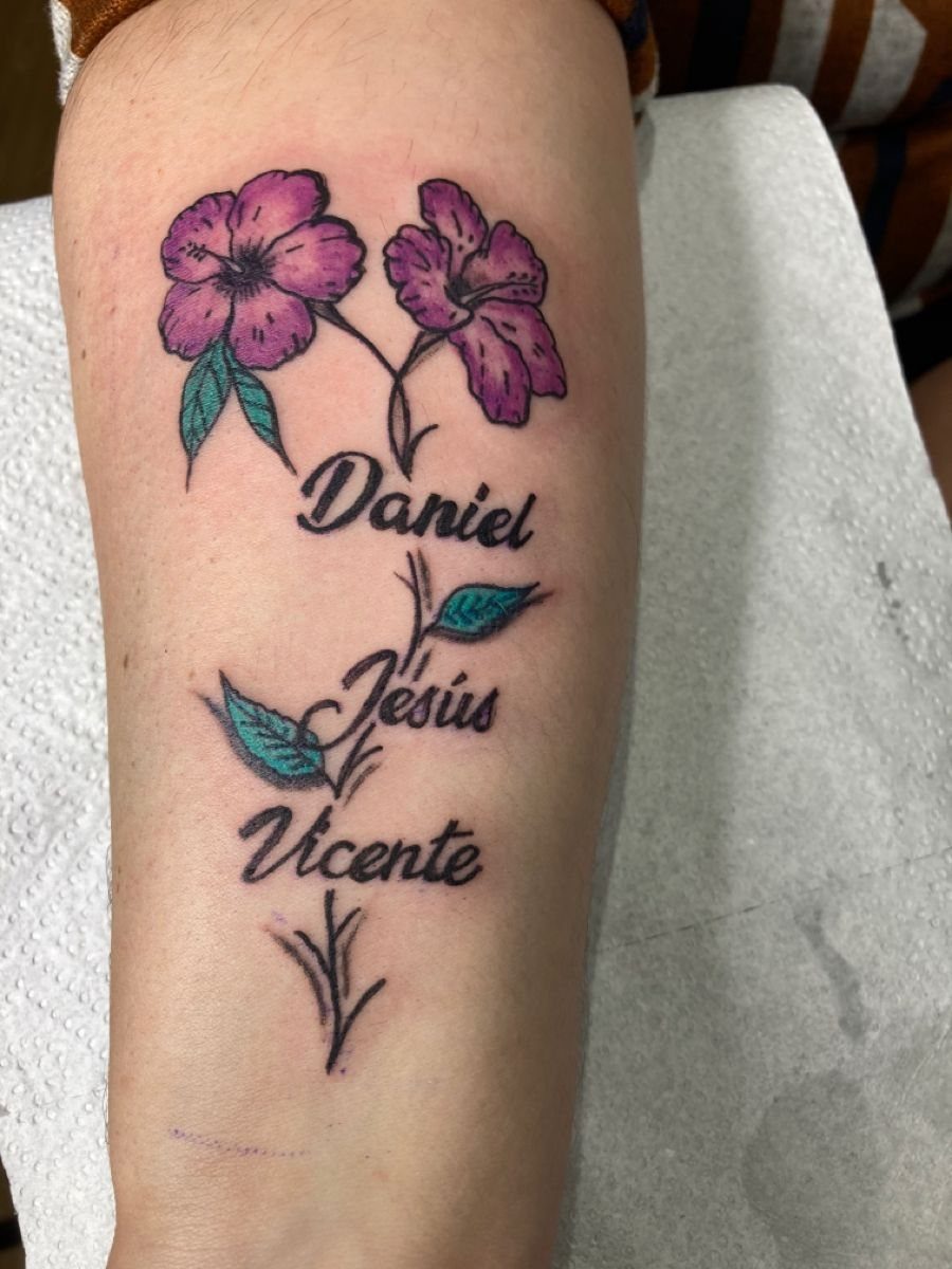 Purple flower tattoo with the names Daniel, Jesus, and Vicente on a forearm