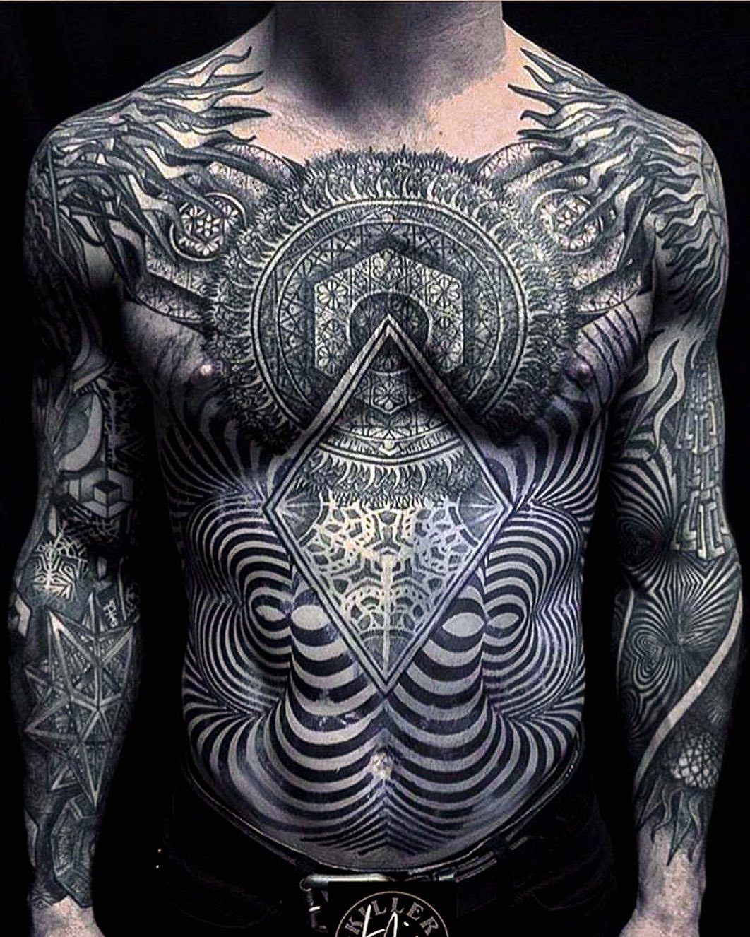 Man's chest and torso covered in intricate circular and linear geometric black tattoos.