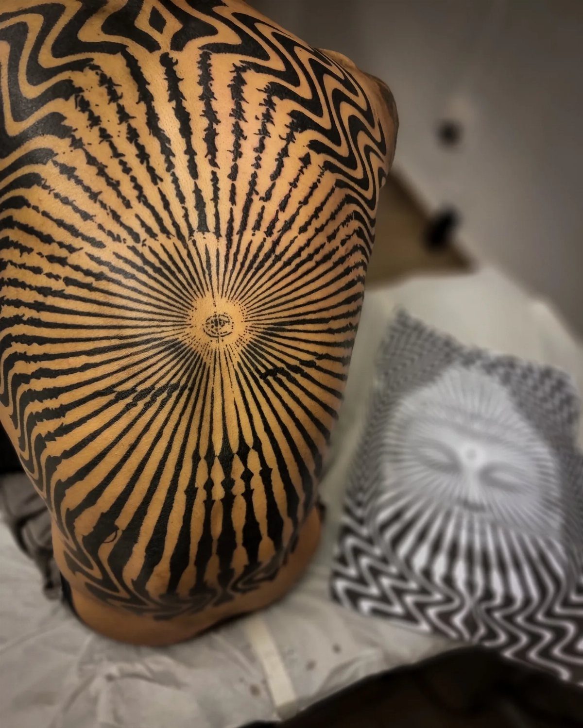 Geometric optical illusion tattoo covering a person's back with radiating black lines.