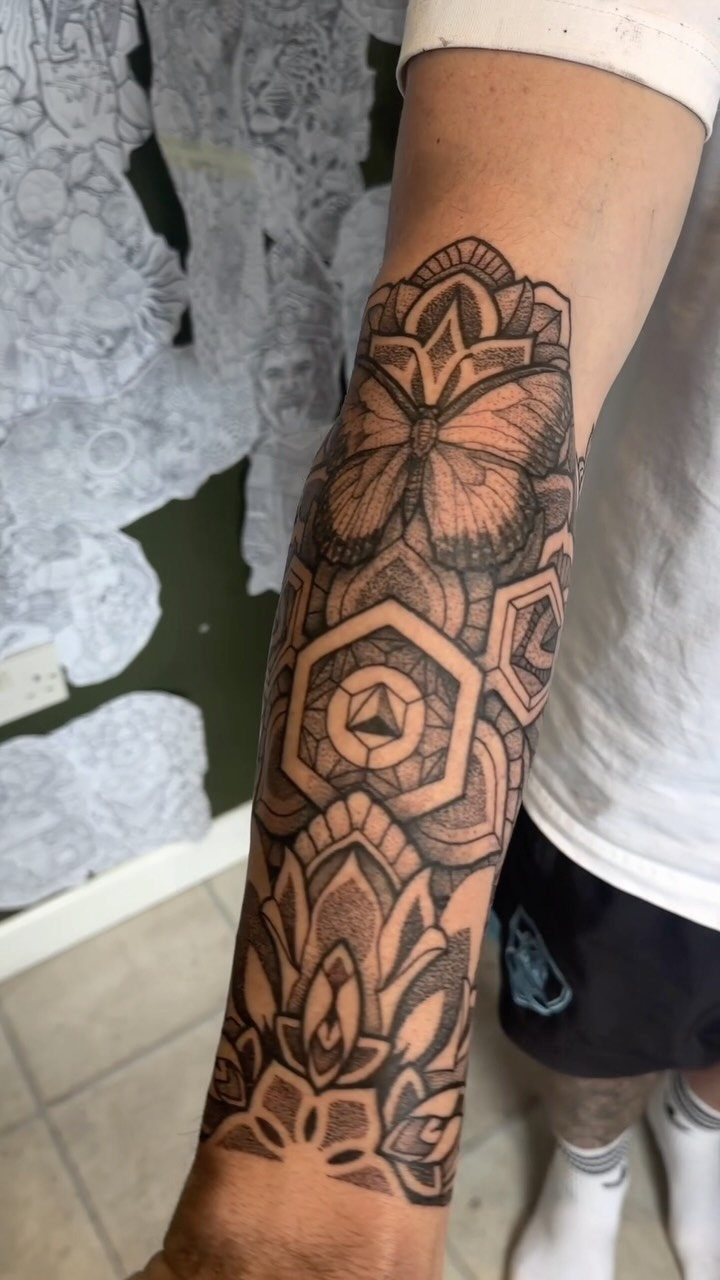 Geometric butterfly tattoo on a forearm surrounded by mandalas and hexagonal patterns.