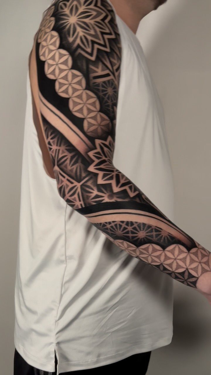 Full sleeve tattoo on an arm featuring intricate black geometric dotwork and mandalas.