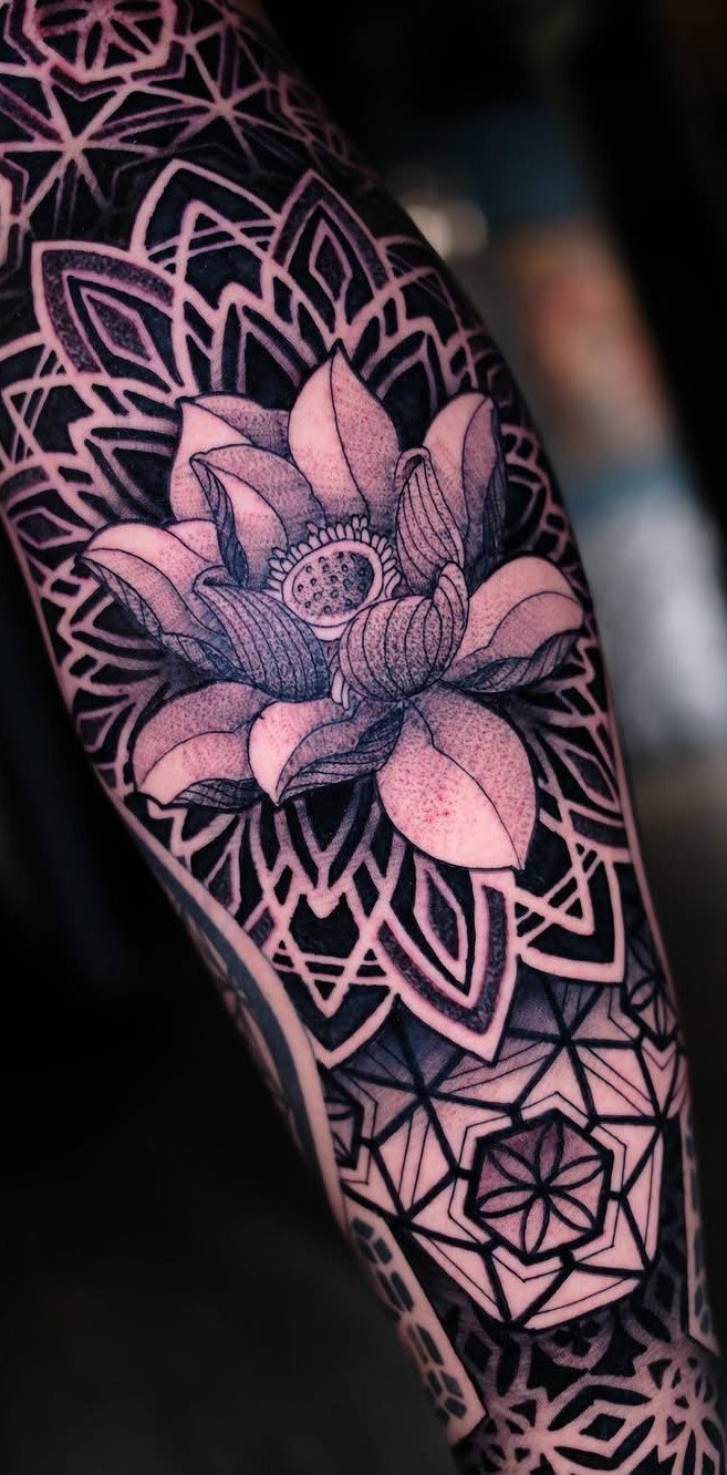 Lotus flower tattoo surrounded by complex geometric patterns and mandalas on an arm.