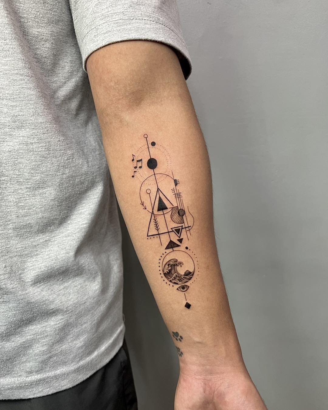 Geometric tattoo on a forearm featuring abstract shapes and a circular ocean wave scene.