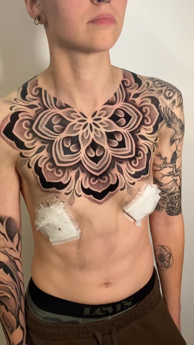 Circular geometric mandala tattoo covering the chest of a person with arm tattoos.