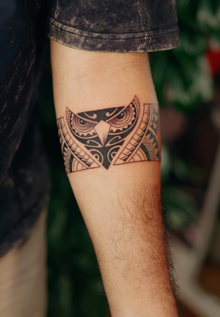Geometric owl tattoo band wrapped around a person's forearm in black ink.