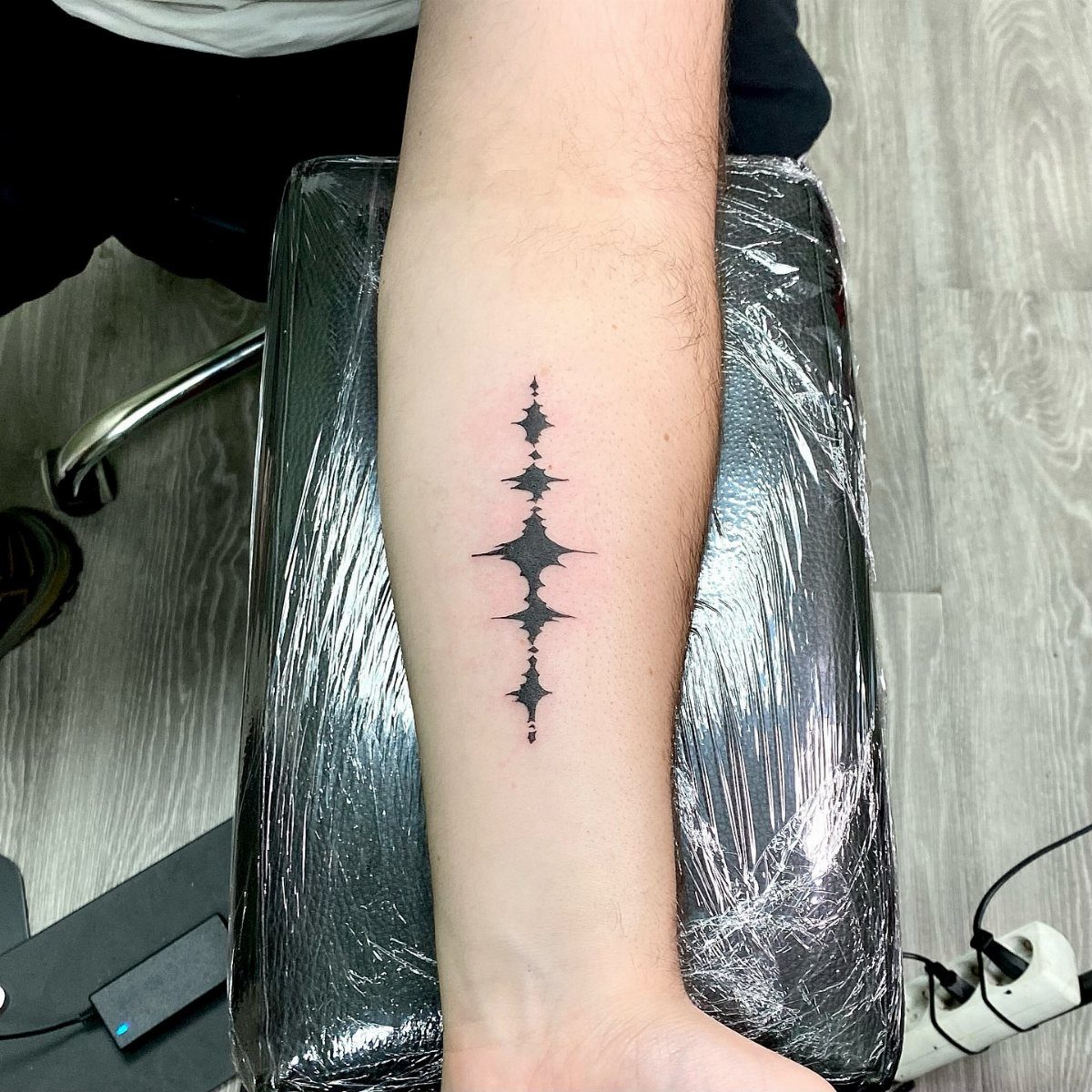 Vertical sound wave tattoo in black ink on a person's inner forearm.