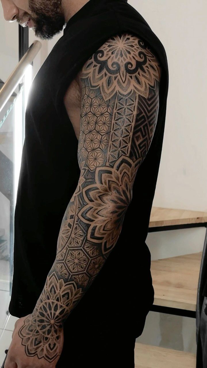 Full sleeve tattoo on a man's arm with intricate black geometric patterns and mandalas.