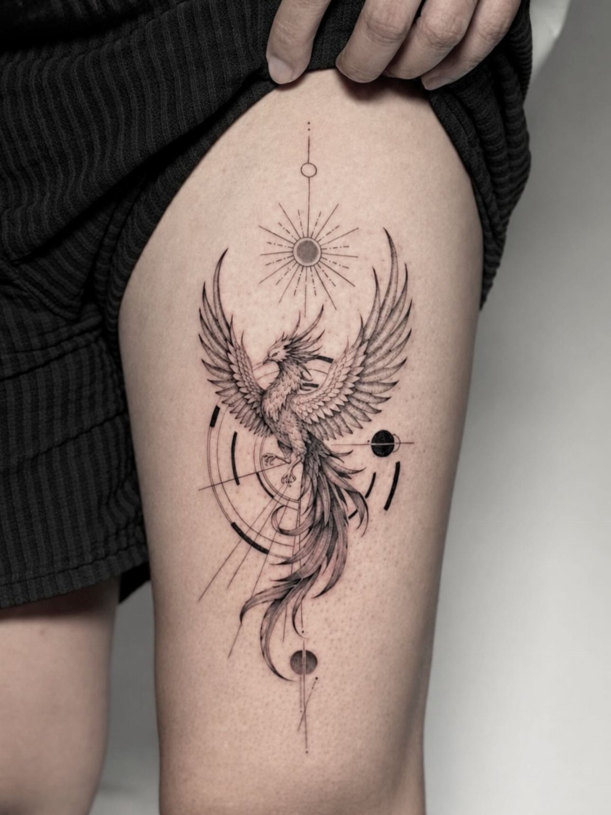 Phoenix tattoo with geometric circles and lines on a person's upper thigh