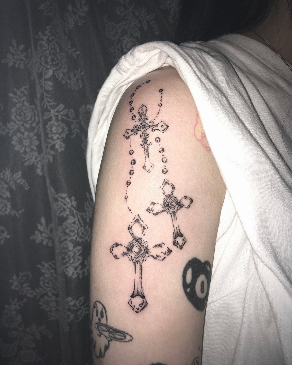 Three gothic cross tattoos on an arm connected by beaded chain lines.