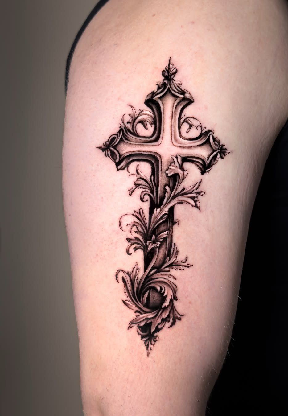 Ornate gothic cross tattoo with floral accents on a person's upper arm