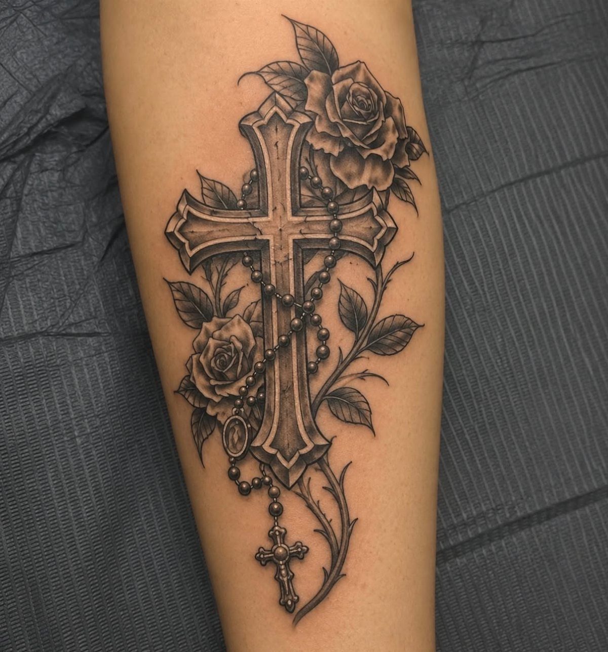 Gothic cross tattoo with roses and a rosary chain on a forearm