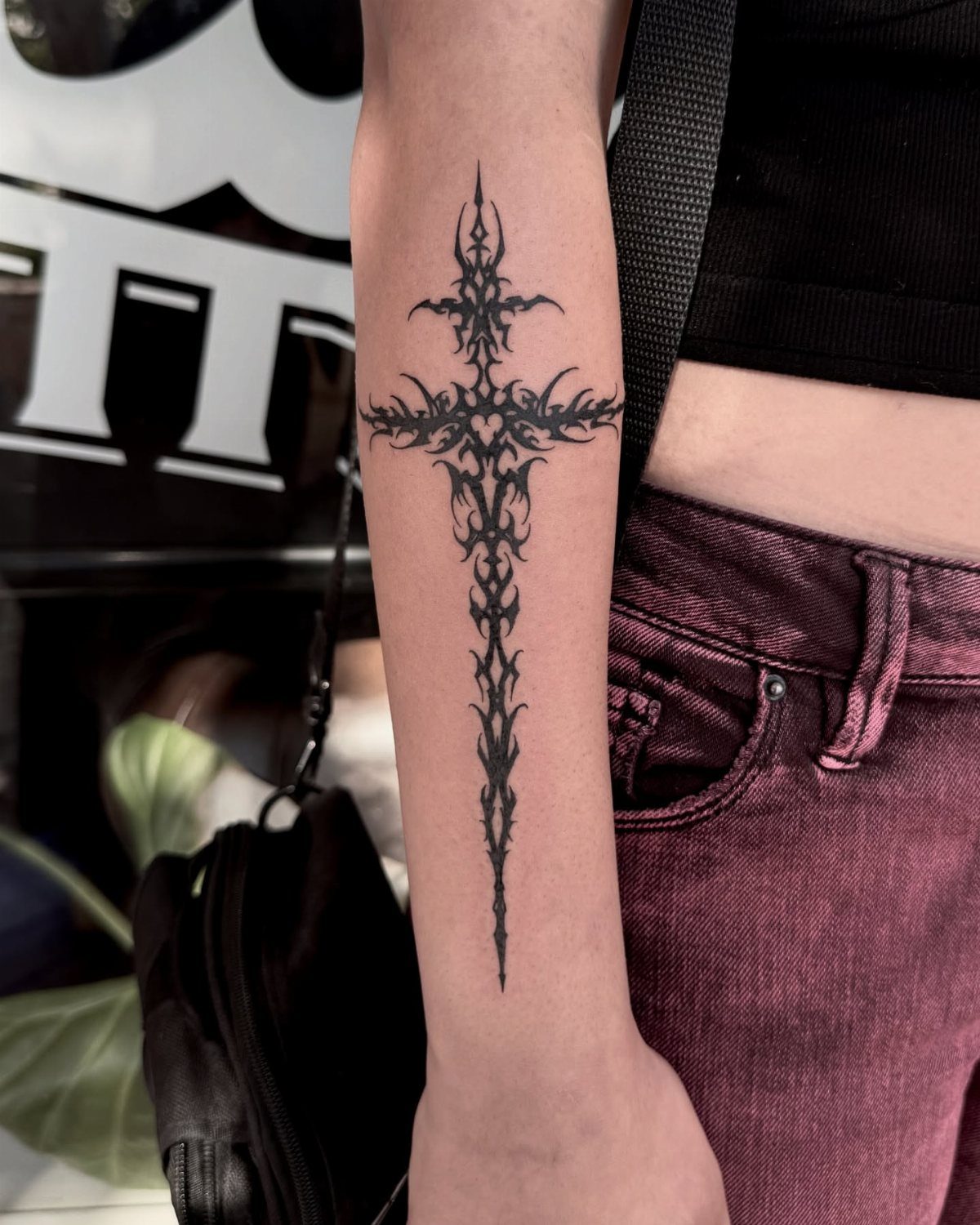 Gothic cross tattoo with tribal flame patterns on a person's forearm