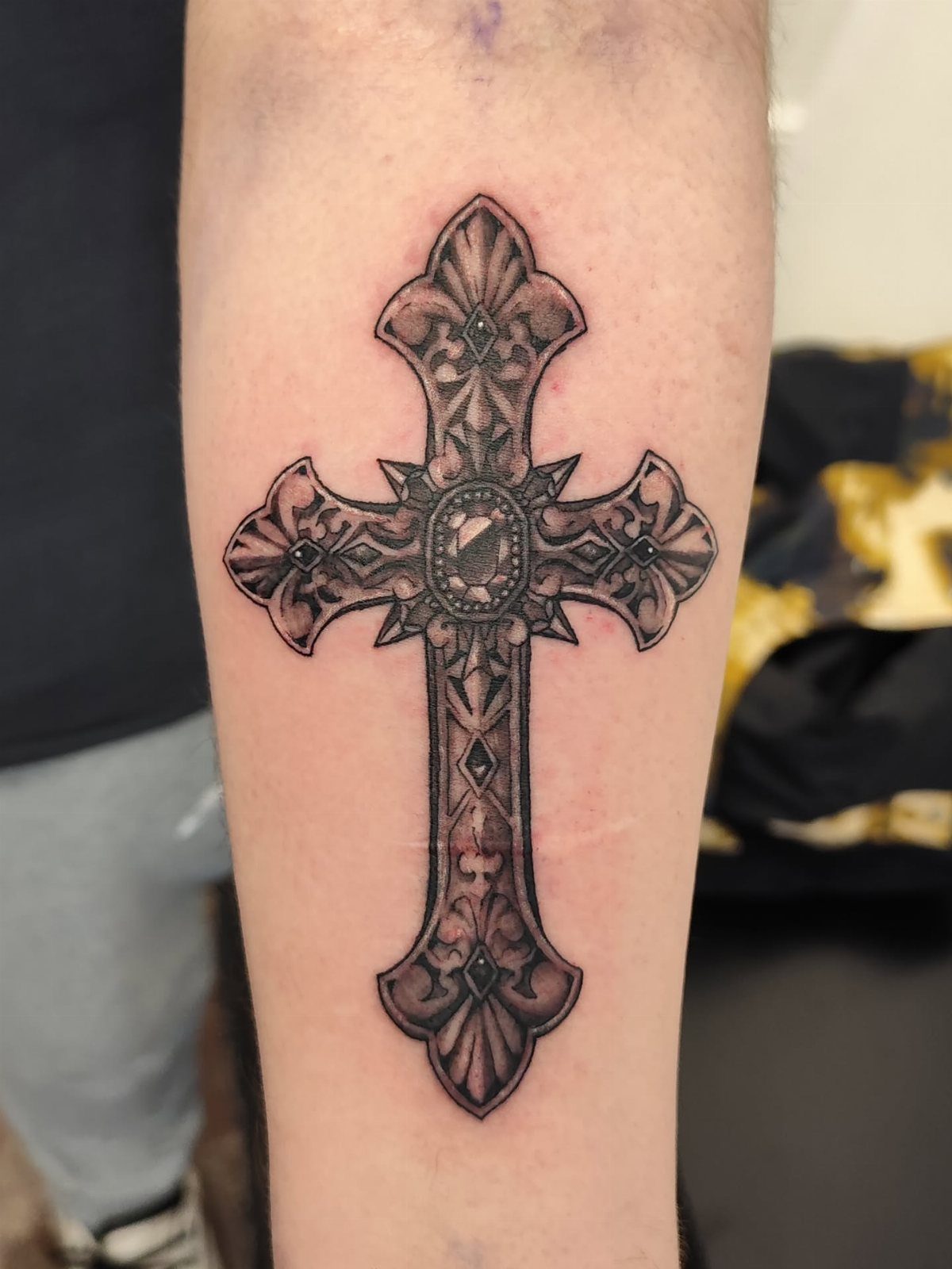 Ornate filigree cross tattoo with intricate gothic patterns on a person's forearm.