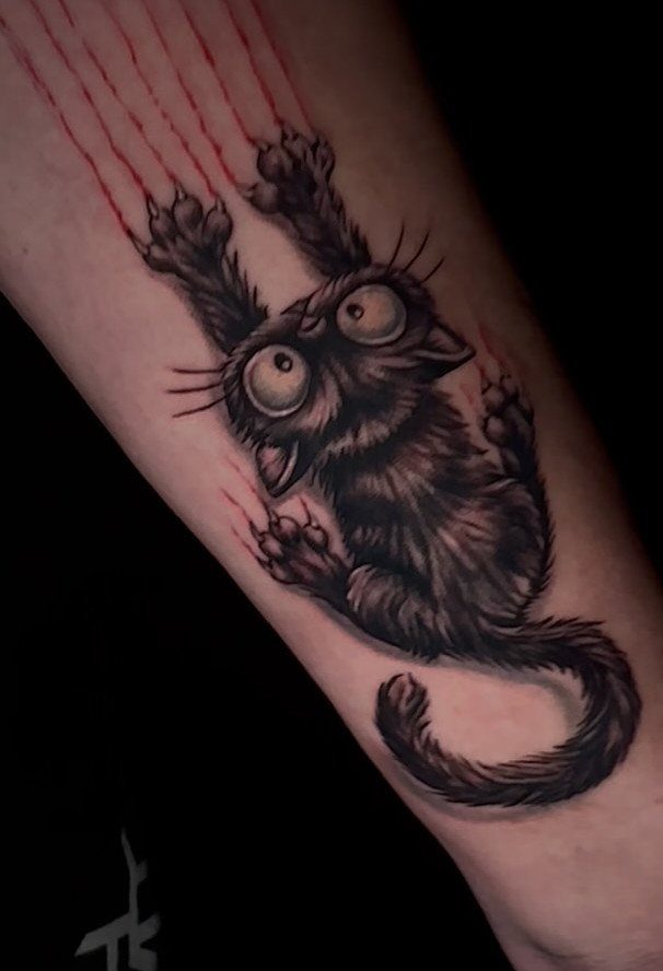 Black cat tattoo with wide eyes and red scratch marks on an arm.