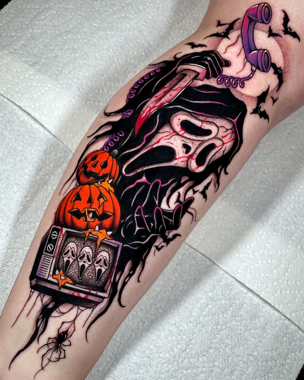 Ghostface tattoo on arm with pumpkins, a knife, and a vintage telephone.