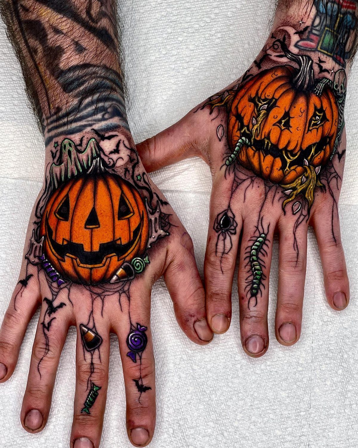 Two hands with detailed orange jack-o'-lantern pumpkin tattoos and Halloween themed imagery.