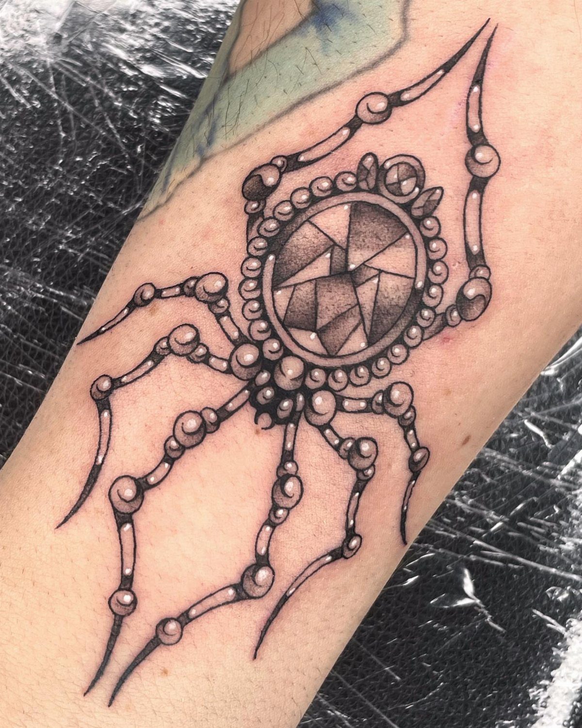 Jeweled spider tattoo with a gemstone body and beaded legs on a person's arm