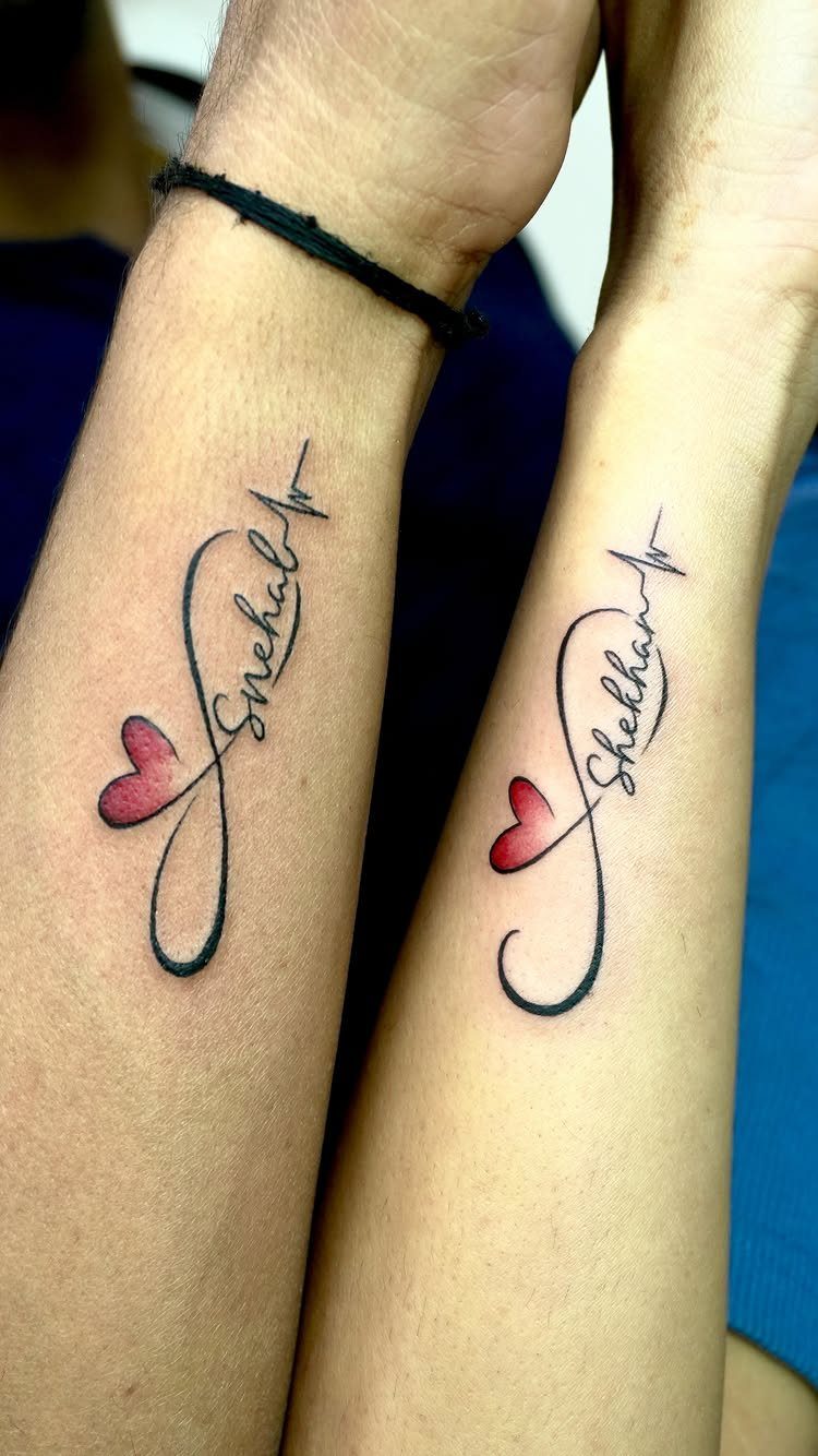 Matching infinity heart tattoos with cursive names and heartbeat lines on two forearms.