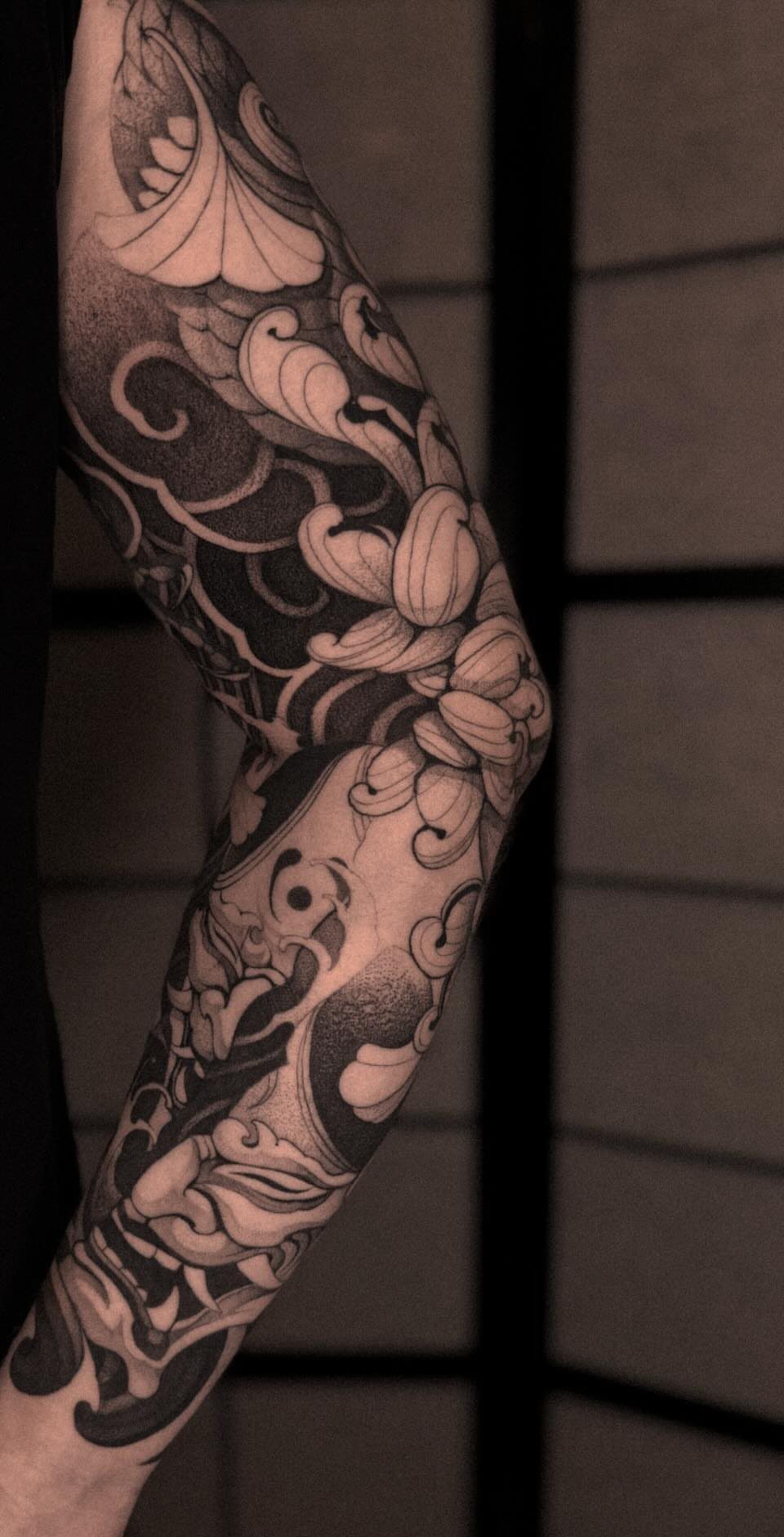 Detailed black and grey Japanese sleeve tattoo with floral motifs on an arm.