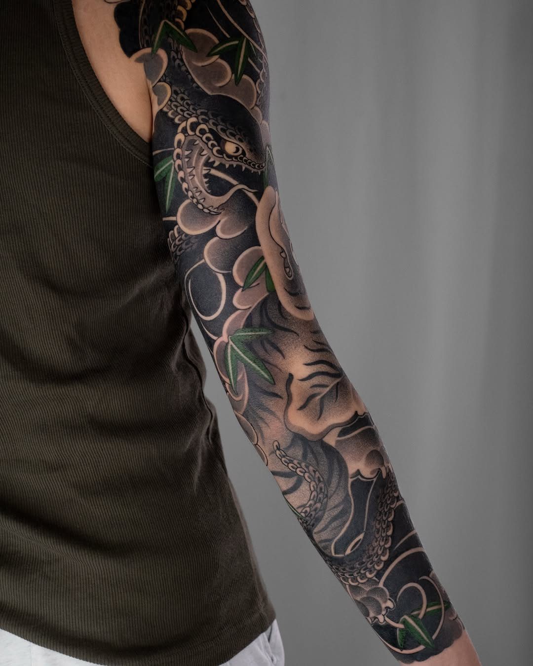 Full sleeve Japanese tattoo on an arm with clouds and green leaves.