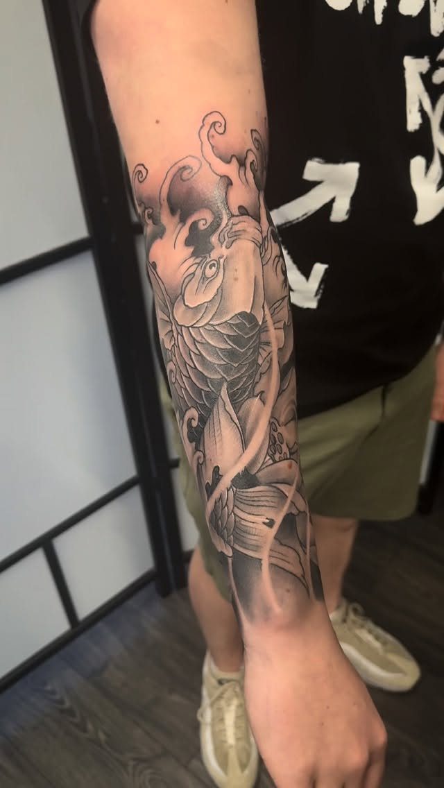 Japanese koi fish tattoo on a person's forearm in black and grey ink