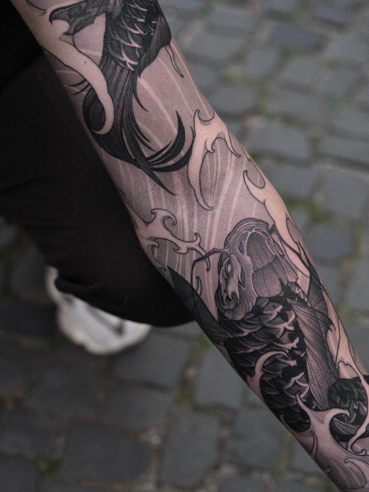 Japanese sleeve tattoo on an arm featuring a koi fish and swirling water.