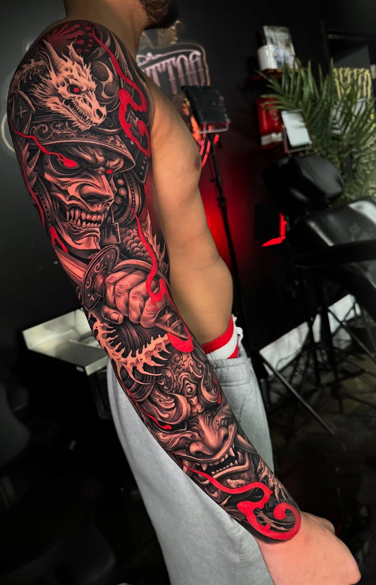 Japanese sleeve tattoo on an arm featuring a samurai mask and red details.