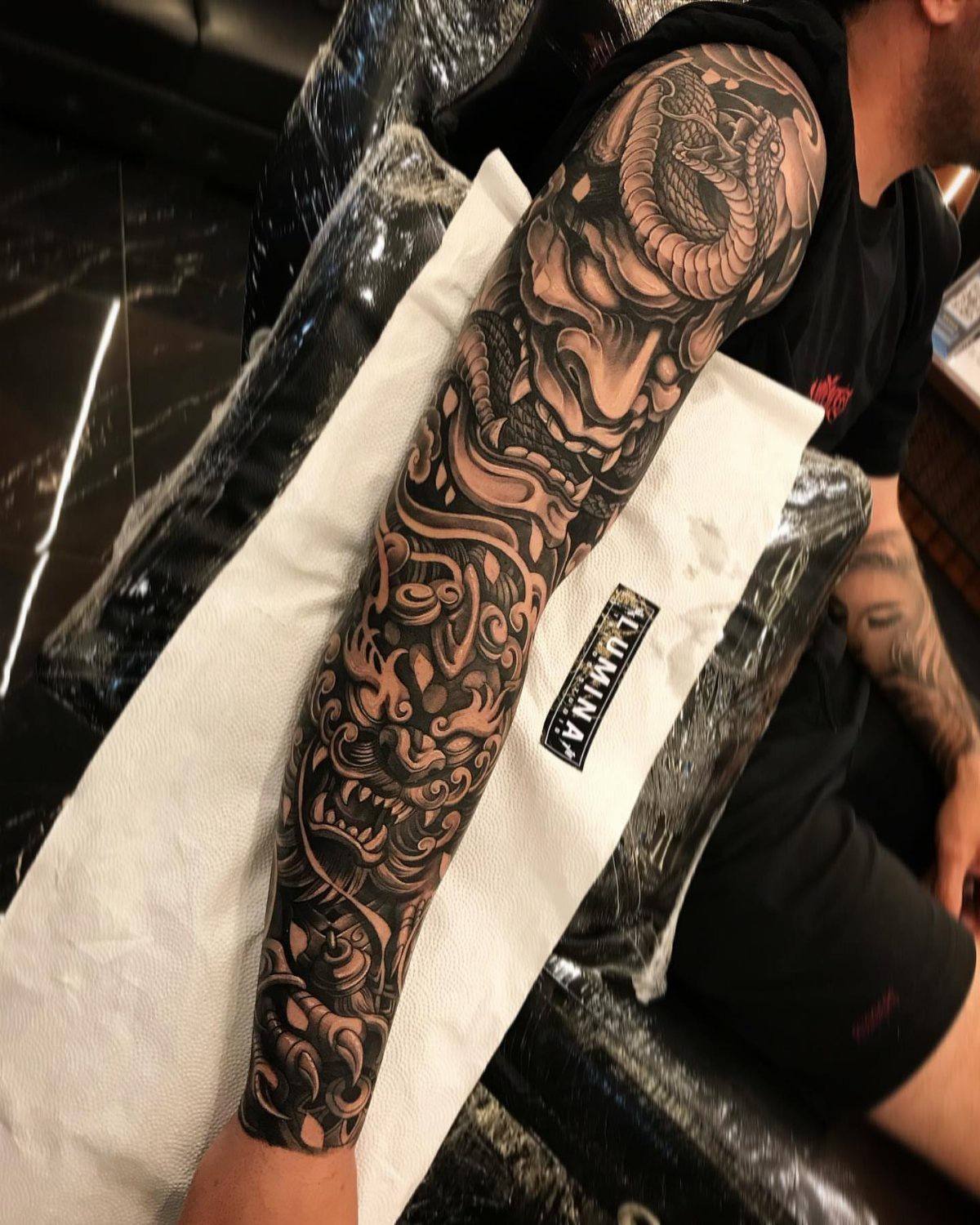 Japanese three-quarter sleeve tattoo with a dragon and demon mask on an arm.