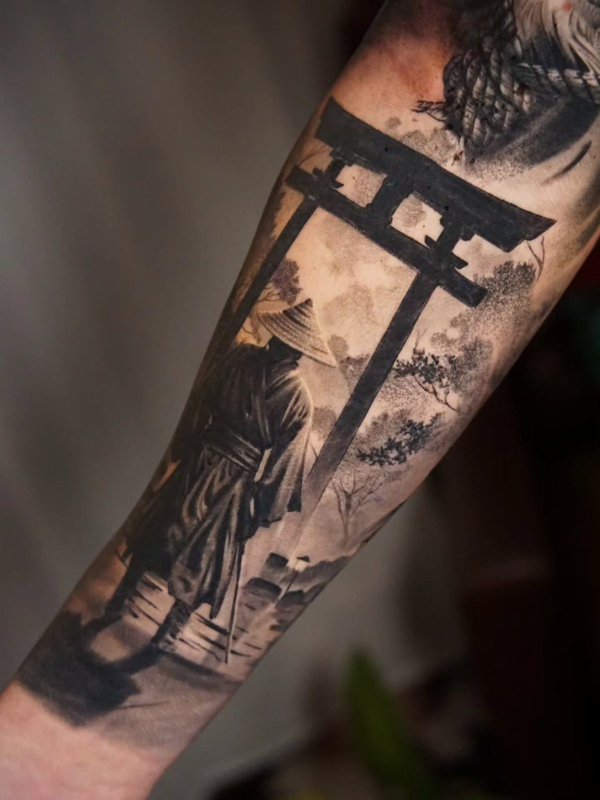 Tattoo on an arm depicting a figure standing before a Japanese torii gate.