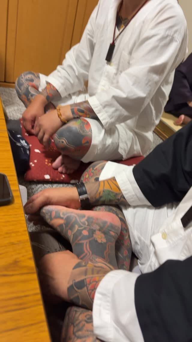 People with extensive traditional Japanese tattoos on their arms and legs sitting indoors.