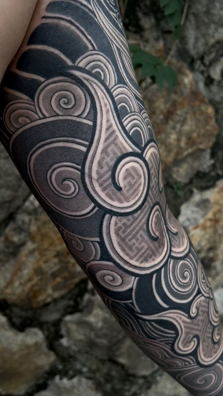 Japanese tattoo pattern with black and grey swirling clouds on a person's arm